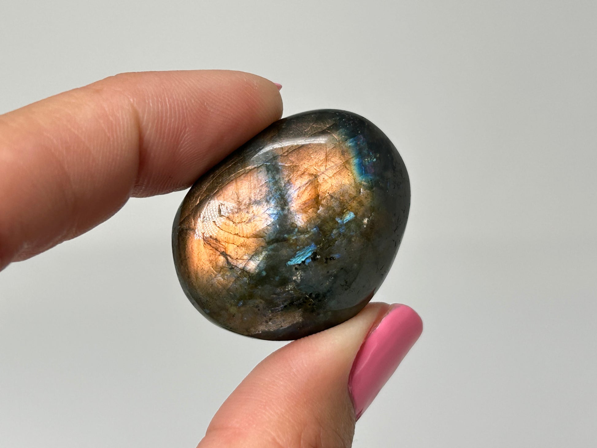 Hand holding a shiny, multicolored Labradorite stone against a plain background