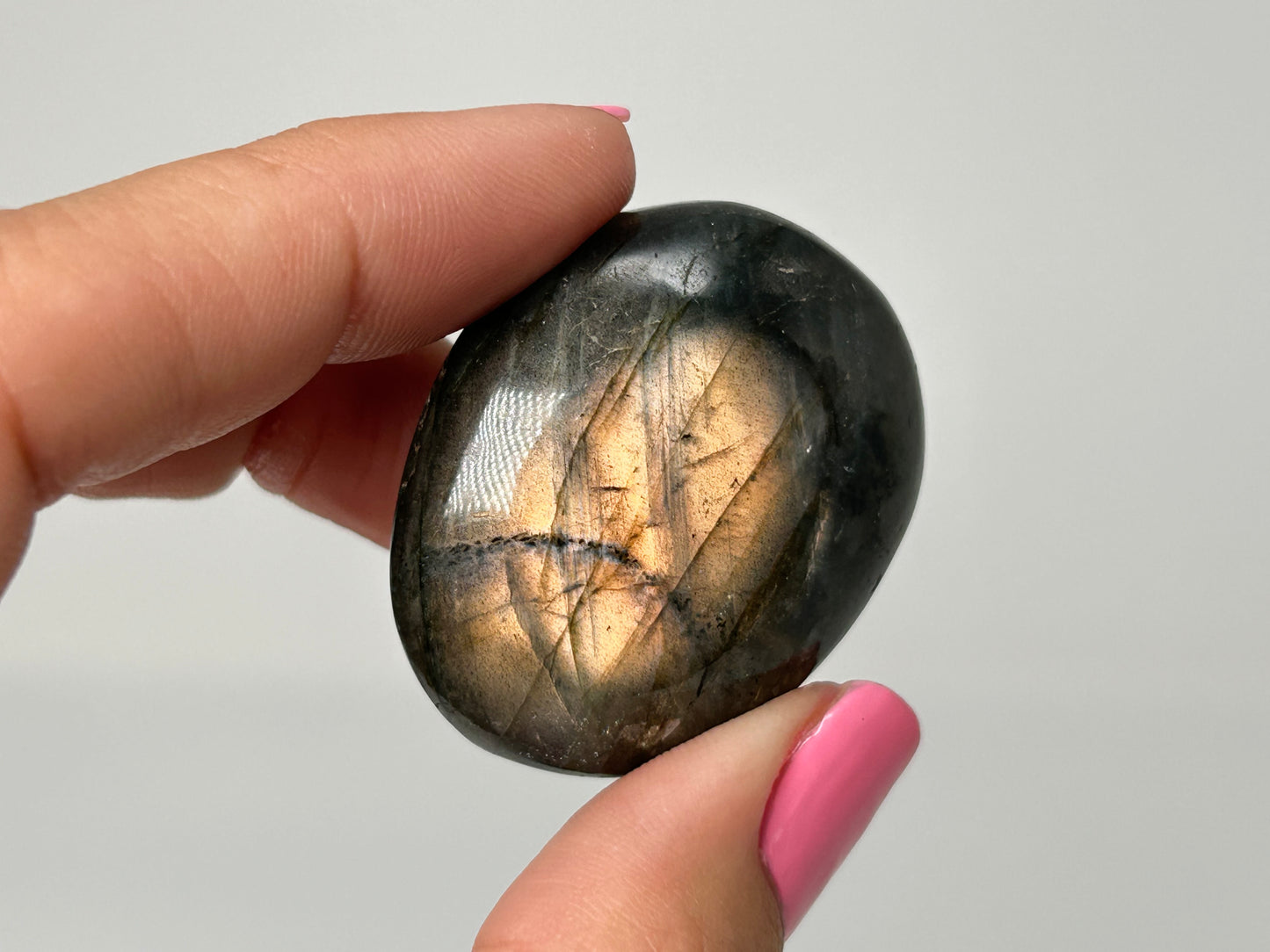 Hand holding a shiny labradorite stone against a plain background