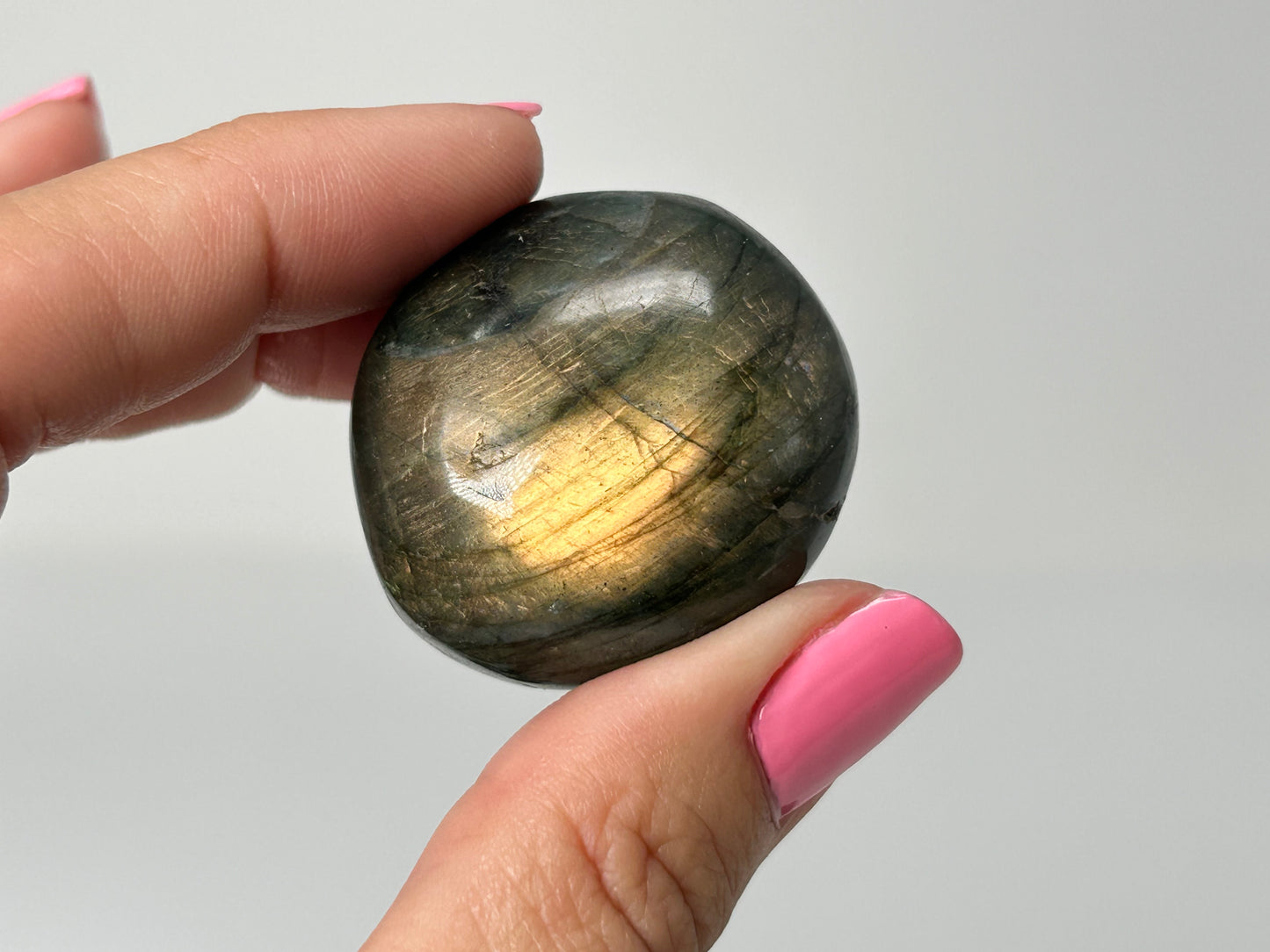 Hand holding a shiny labradorite stone against a plain background