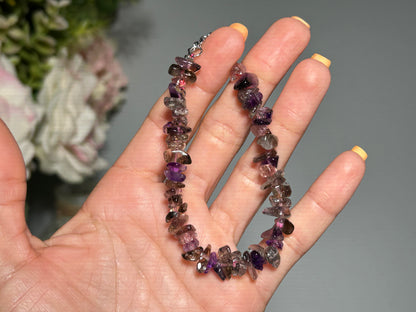 Hand holding a Super 7 Chip Bead Bracelet for meditation and energy work with a blurred floral background