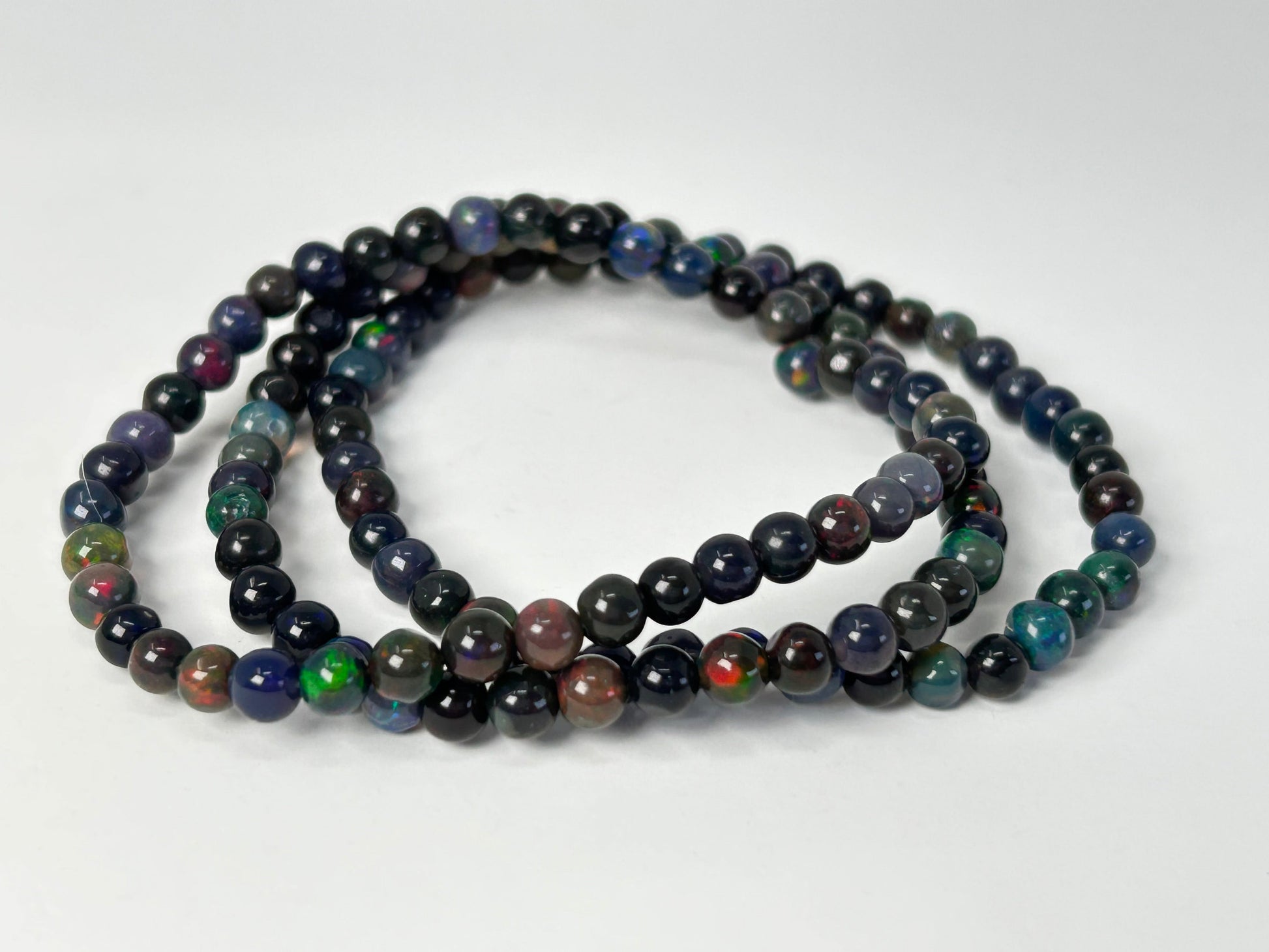 Three Transformative Black Opal Bracelets with multicolored stones on a white background
