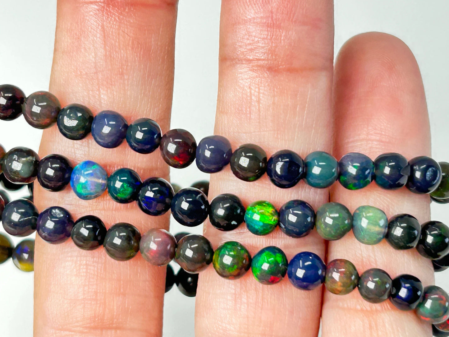 Close-up of a hand holding strands of multicolored black opal beaded bracelets.