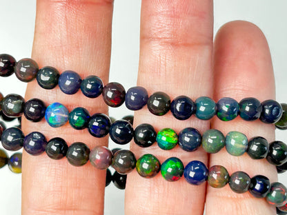 Close-up of a hand holding strands of multicolored black opal beaded bracelets.