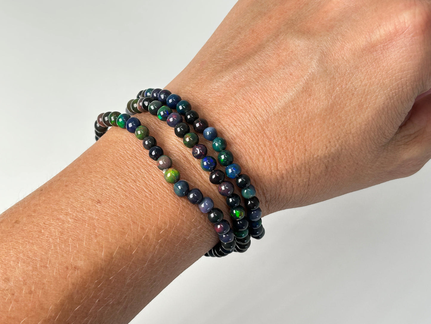 Beaded black opal bracelets on a wrist against a neutral background