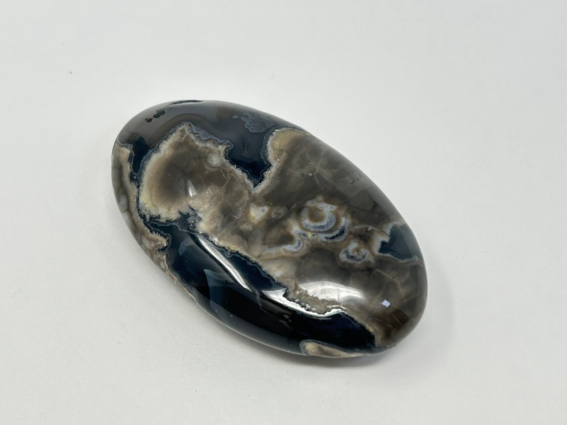 A polished oval Volcano Agate Crystal Healing Palm Stone with natural marbled patterns of black, gray, and white, displayed on a clean white background.