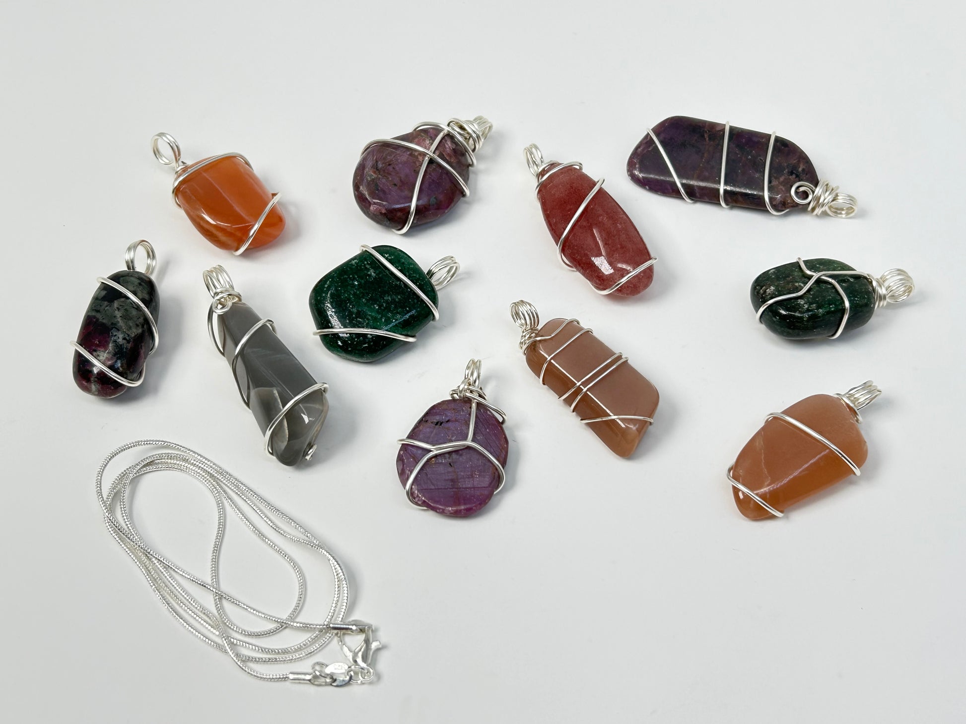 Wire Wrapped Crystal Pendants for natural grounding and silver necklace chain on table with white background.