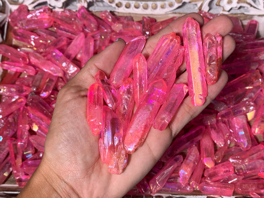 A collection of pink aura quartz points held in a person's hand, with more quartz points visible in the background.