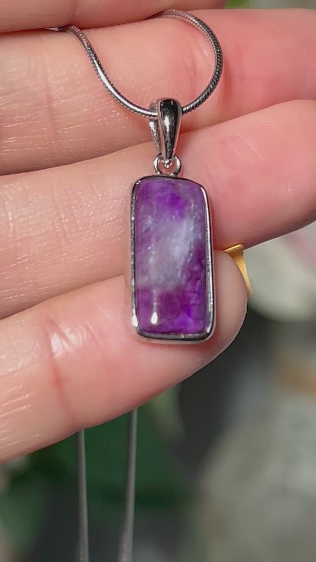 Video of hand holding a Purple Sugilite Crystal Pendant in Sterling Silver with white gray and floral background.