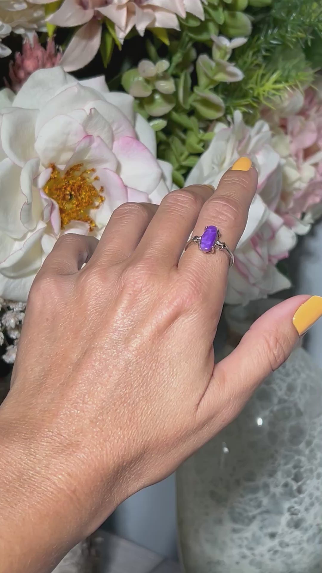 Video of hand wearing a Purple Sugilite Crystal in Sterling Silver Ring with Cubic Zirconia with white gray and floral background.