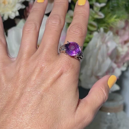 Hand wearing a Amethyst Evil Eye Ring in Sterling Silver with blurred floral background.