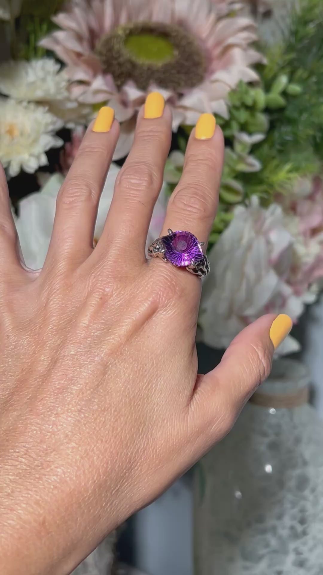 Hand wearing a Amethyst Evil Eye Ring in Sterling Silver with blurred floral background.