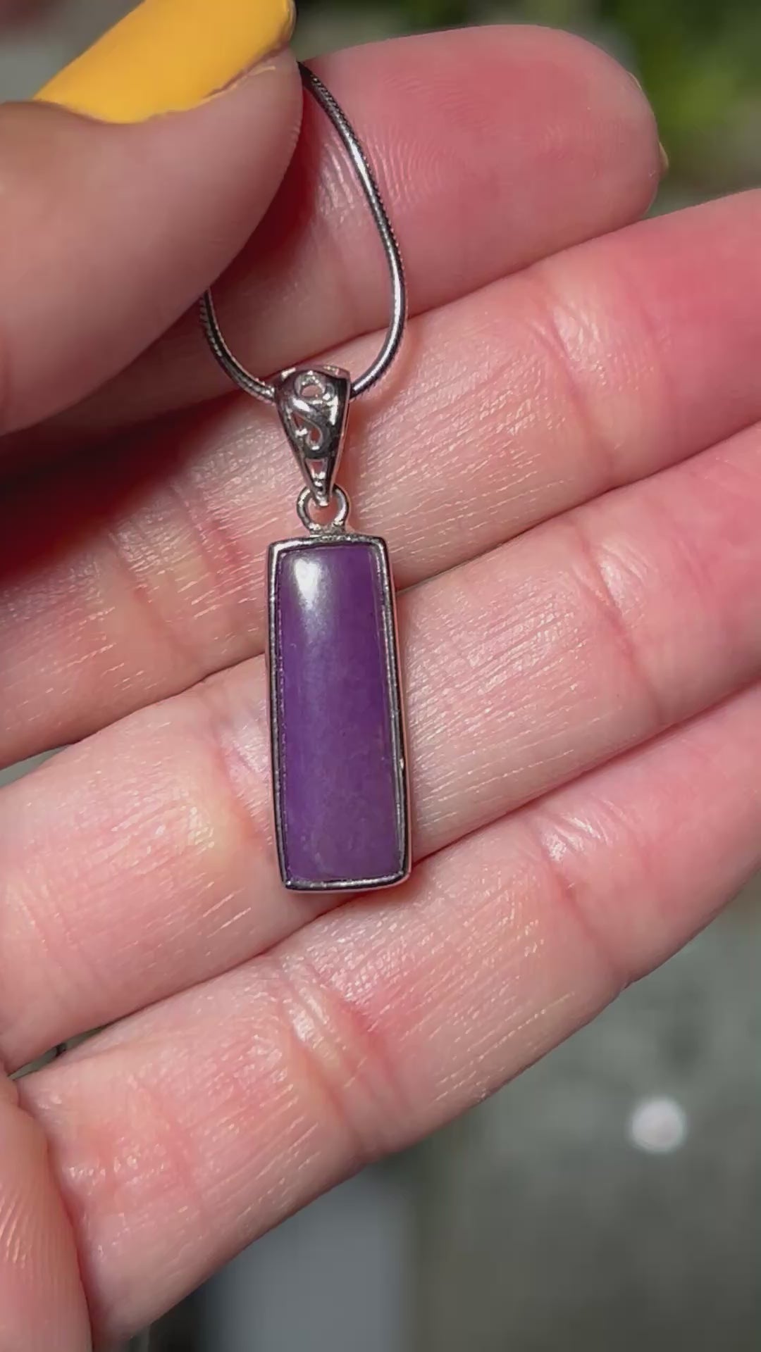 Video of hand holding a Sugilite Sterling Silver Pendant on a silver chain with floral background.