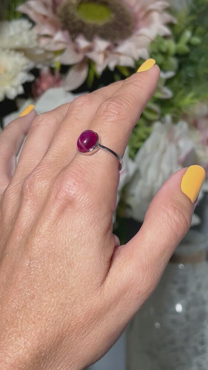 Hand wearing a Star Ruby and Sterling Silver Ring with floral background.