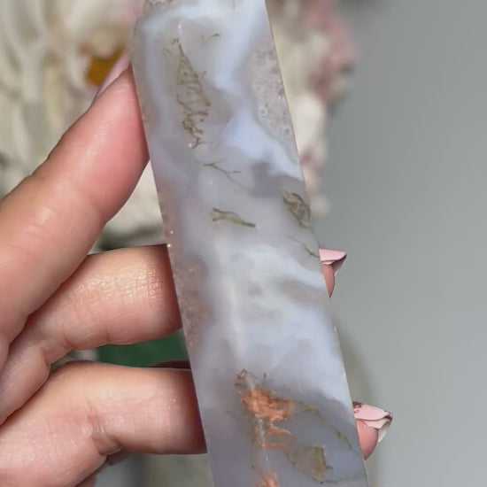 Video of hand holding a Moss Agate Crystal Tower with white gray floral background.
