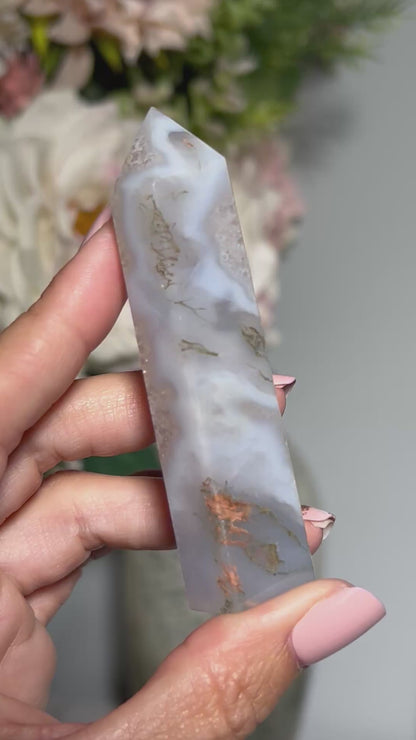 Video of hand holding a Moss Agate Crystal Tower with white gray floral background.