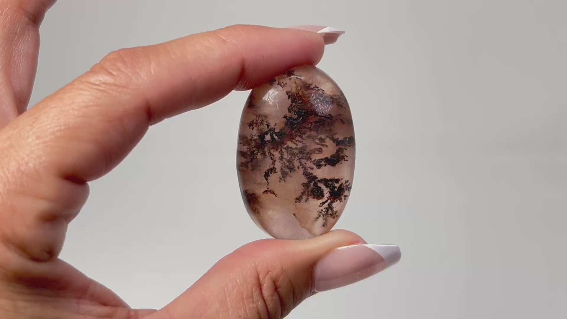 Hand holding a beautiful Oval-shaped Brown Dendritic Fluorite ethically sourced natural healing crystal gemstone for meditation over white background.