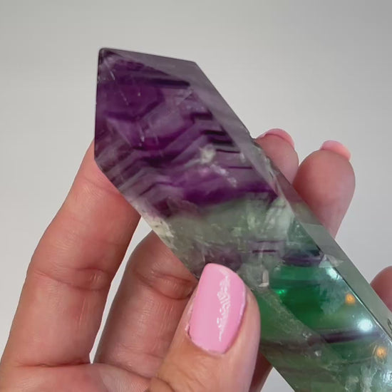 Video of hand holding a Rainbow Fluorite Tower gemstone with white background.