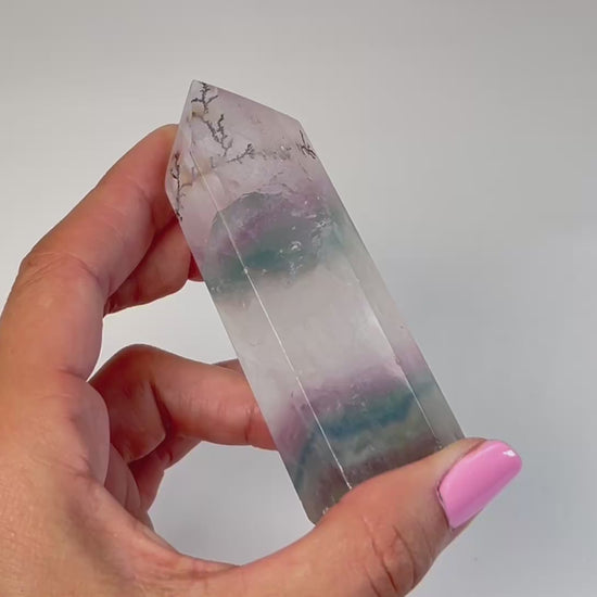 Video of hand holding a Dendritic Fluorite Tower gemstone with white background.