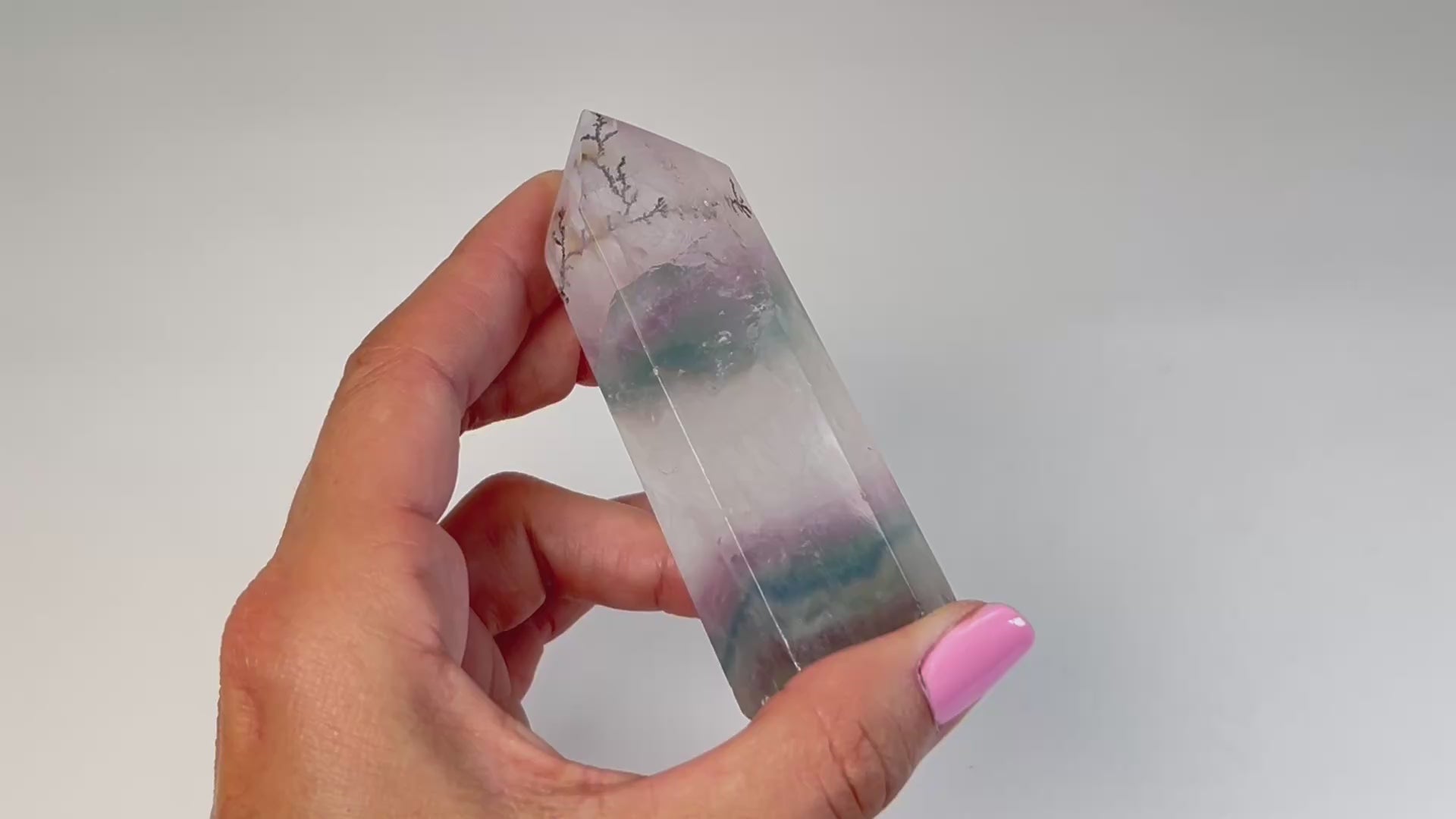 Video of hand holding a Dendritic Fluorite Tower gemstone with white background.