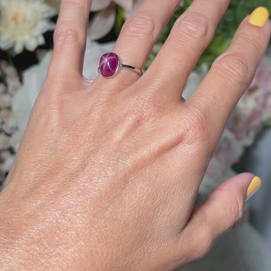 Hand wearing a Star Ruby Ring in Sterling Silver with gray and floral background.
