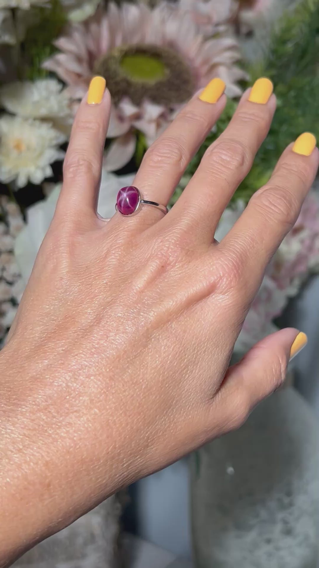 Hand wearing a Star Ruby Ring in Sterling Silver with gray and floral background.
