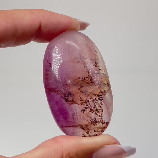 Hand holding a Oval-shaped Brown Organic Dendritic Fluorite Palm Stone chakra balancing gemstone for spiritual healing crystal against white background.