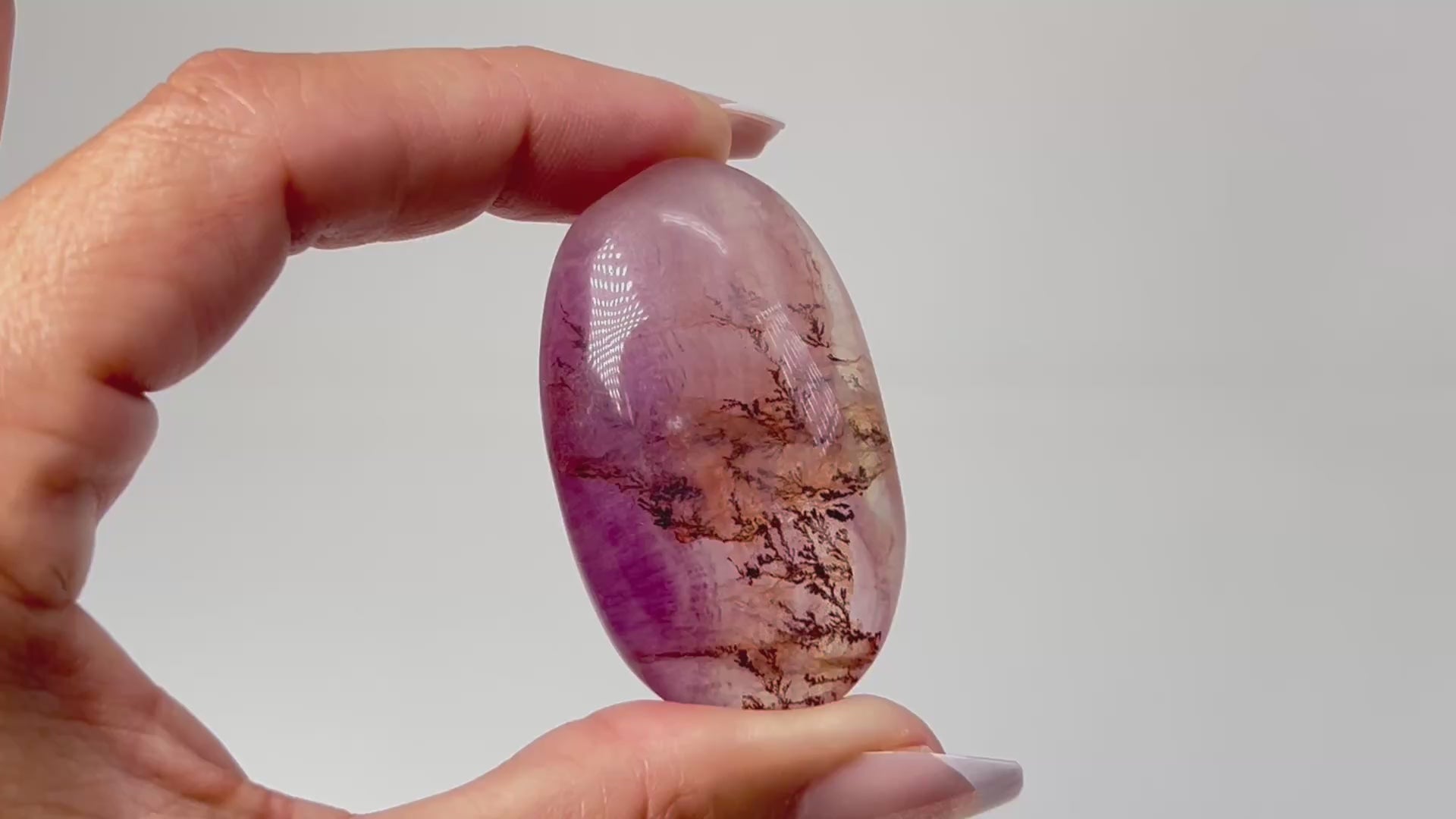 Hand holding a Oval-shaped Brown Organic Dendritic Fluorite Palm Stone chakra balancing gemstone for spiritual healing crystal against white background.