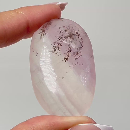 Hand holding Oval-shaped Dendritic Fluorite healing gemstone on table with white background.
