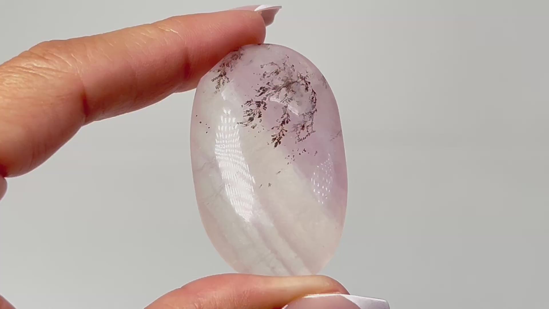 Hand holding Oval-shaped Dendritic Fluorite healing gemstone on table with white background.