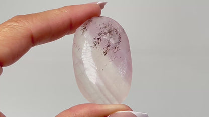 Hand holding Oval-shaped Dendritic Fluorite healing gemstone on table with white background.
