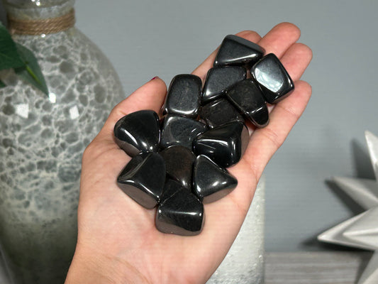 A person holding a cluster of tumbled Hematite stones for grounding protection in their palm.